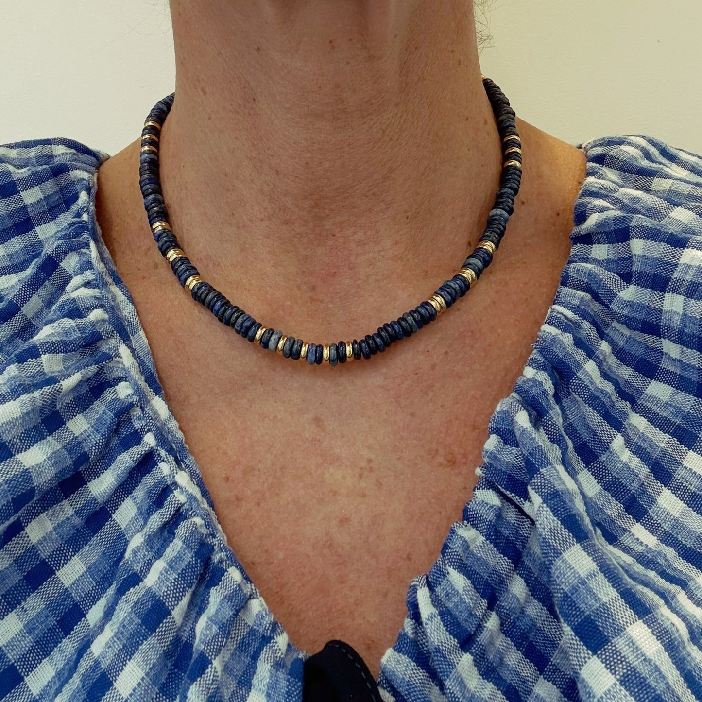Person wearing a blue and gold beaded necklace with a blue checkered garment.
