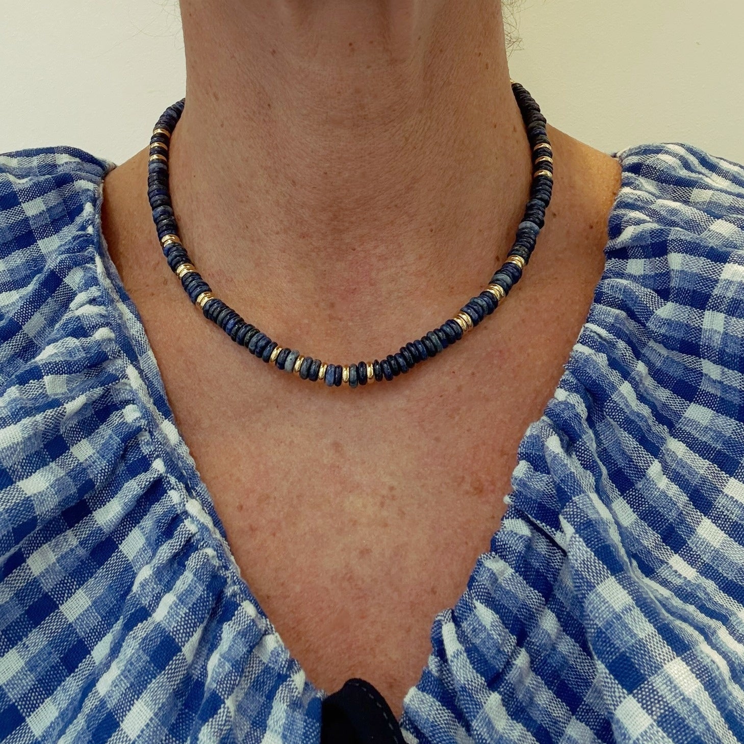 Person wearing a blue and gold beaded necklace with a blue checkered garment.