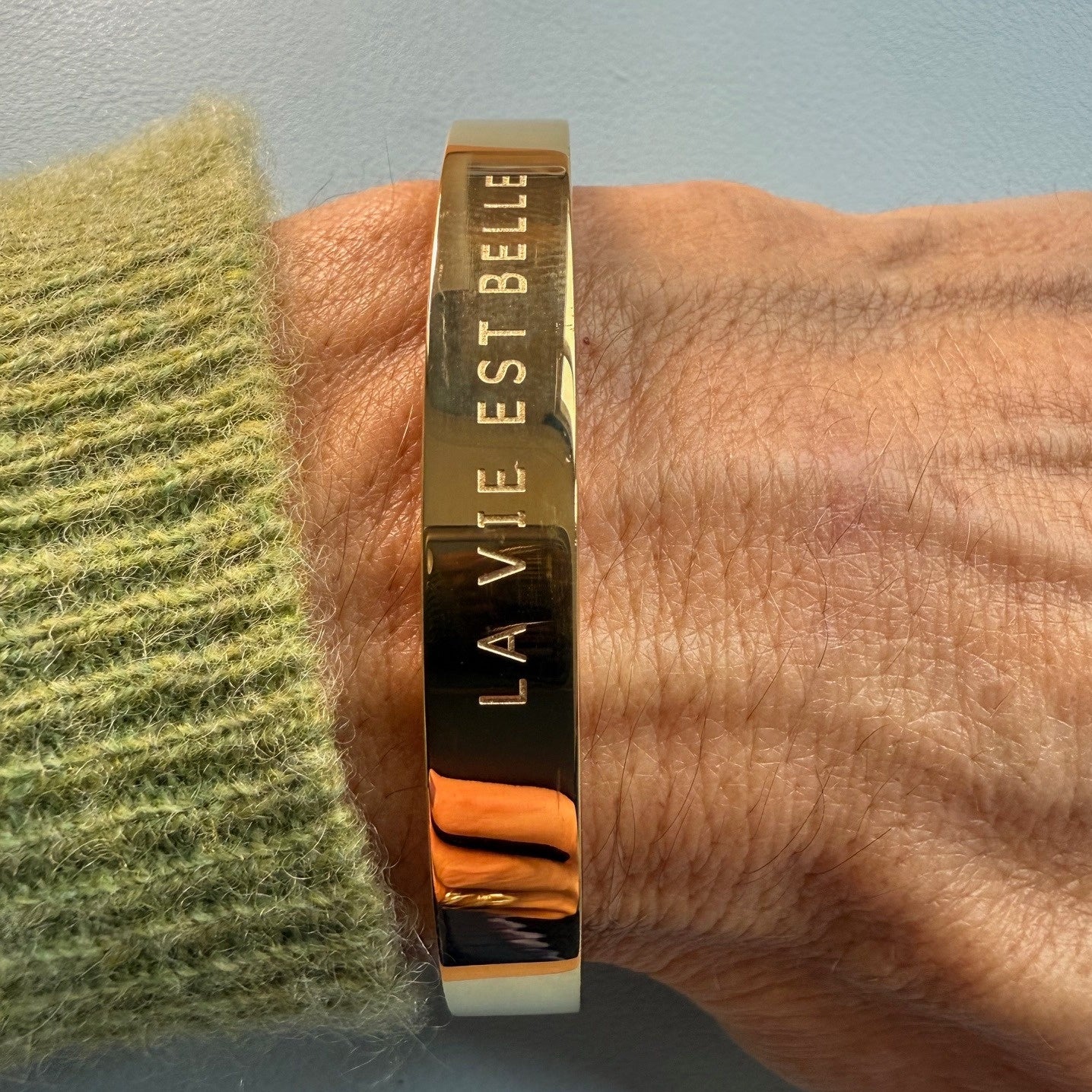 gold bangle which is engraved with the phrase: La Vie Est Belle - life is beautiful! On model