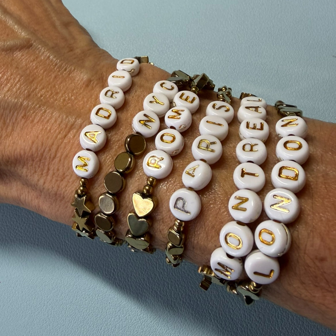 Stretchy bracelets with city names in  gold letters on white beads and small Hematite  beads all around