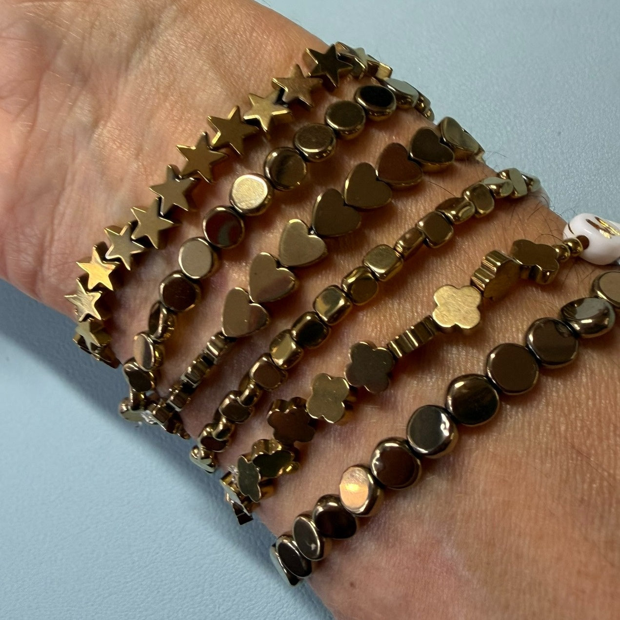 Gold beaded bracelets on a wrist against a light blue background