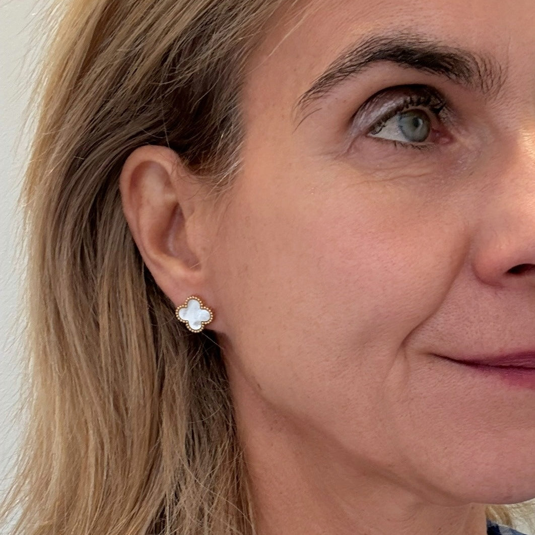 Close-up of a woman wearing a gold and mother of pearl clover shaped earring.