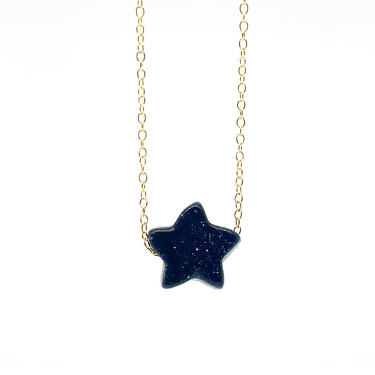 Delicate gold chain necklace with one star-shaped flat stone charm in sparkly midnight blue