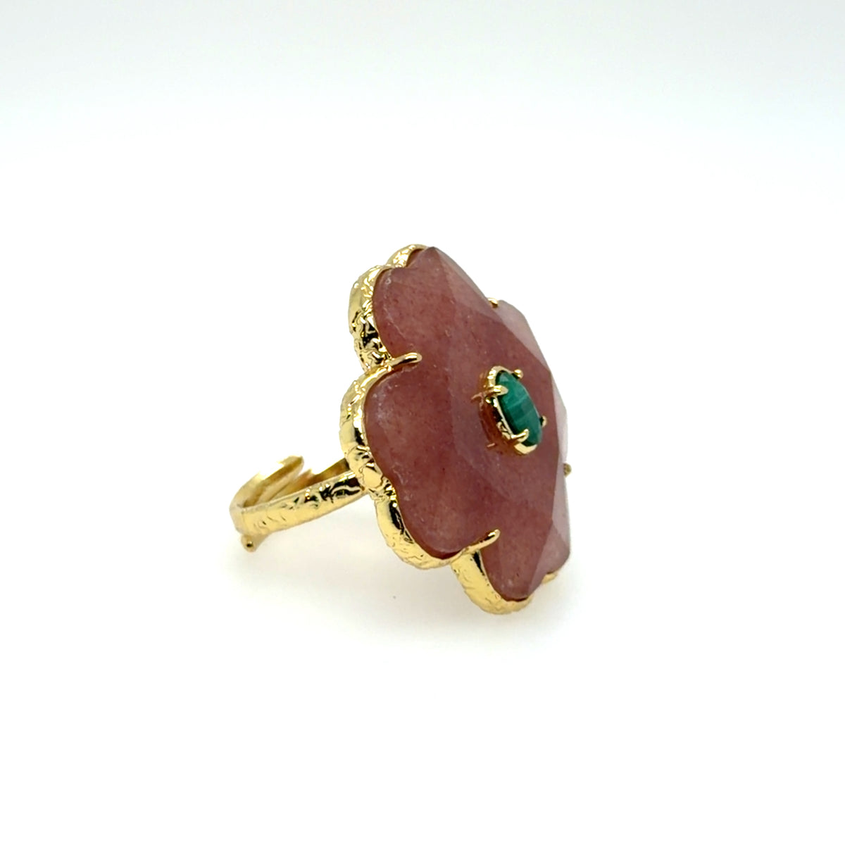 A gold ring featuring a large, scalloped pinkish-red stone with a small green emerald-cut center, set against a plain white background.