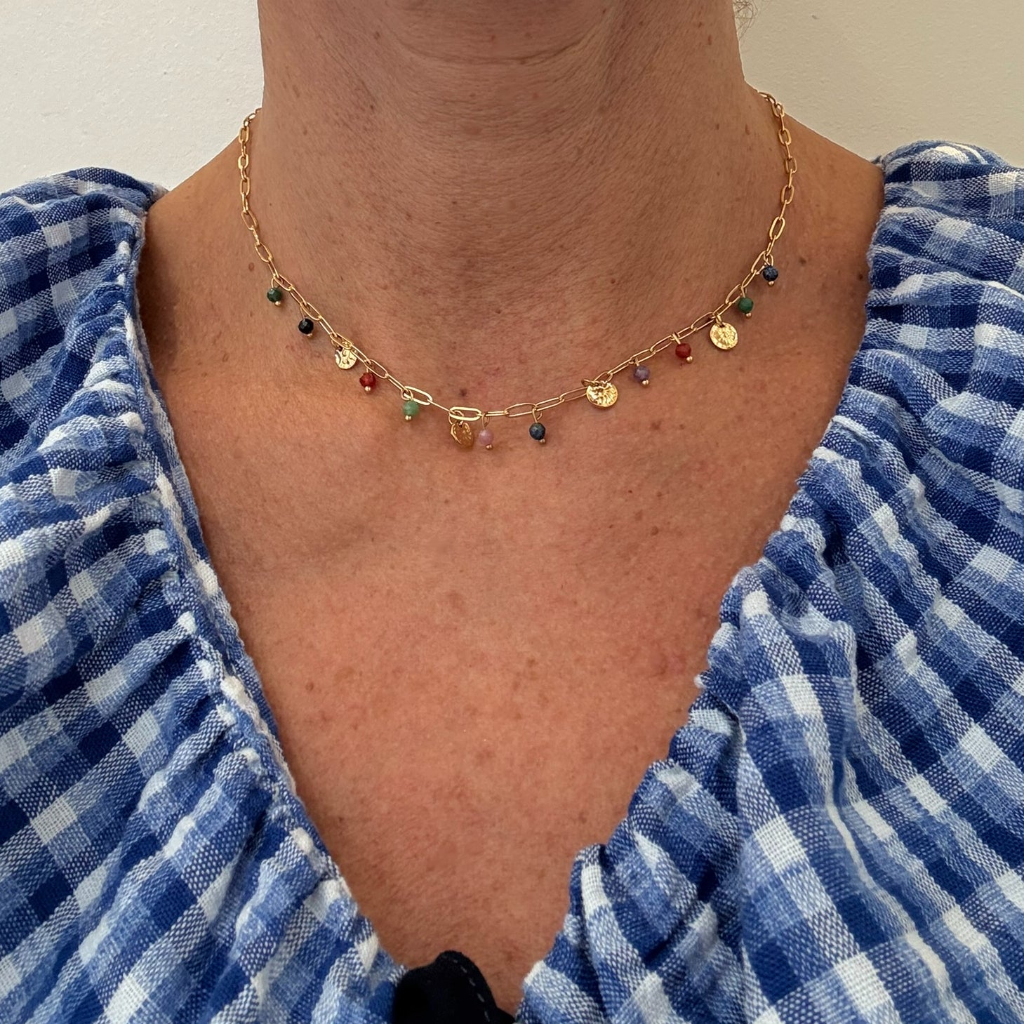 Gold paperclip style necklace with dangling little discs and beads in a rainbow of colours worn on woman