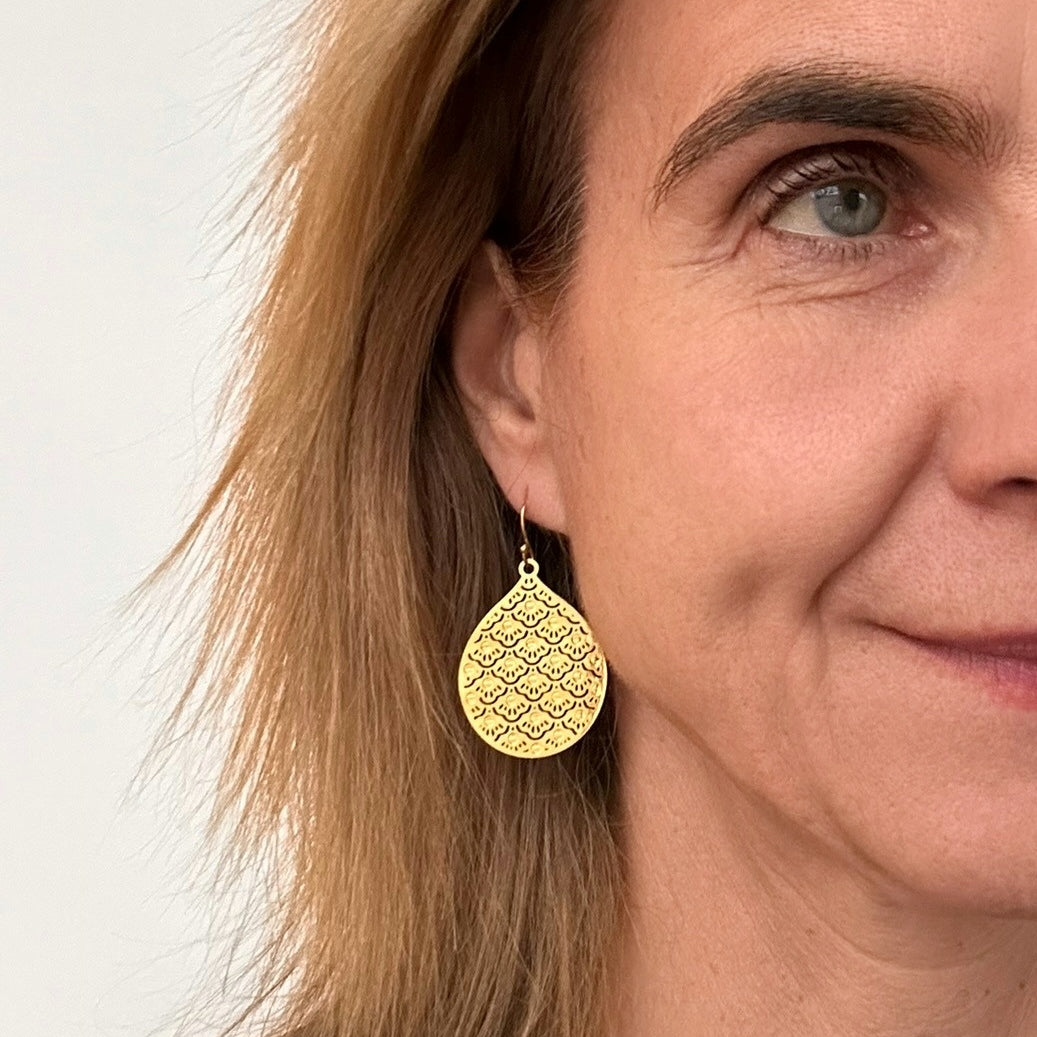 Small patterned shimmery gold teardrop earrings on model