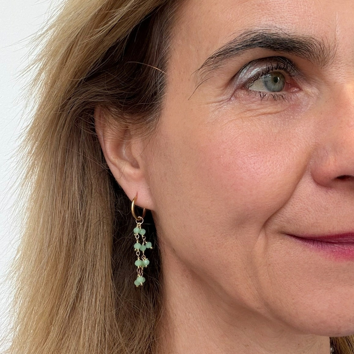 Close-up of a woman wearing green prehnite gemstone earrings with a plain background