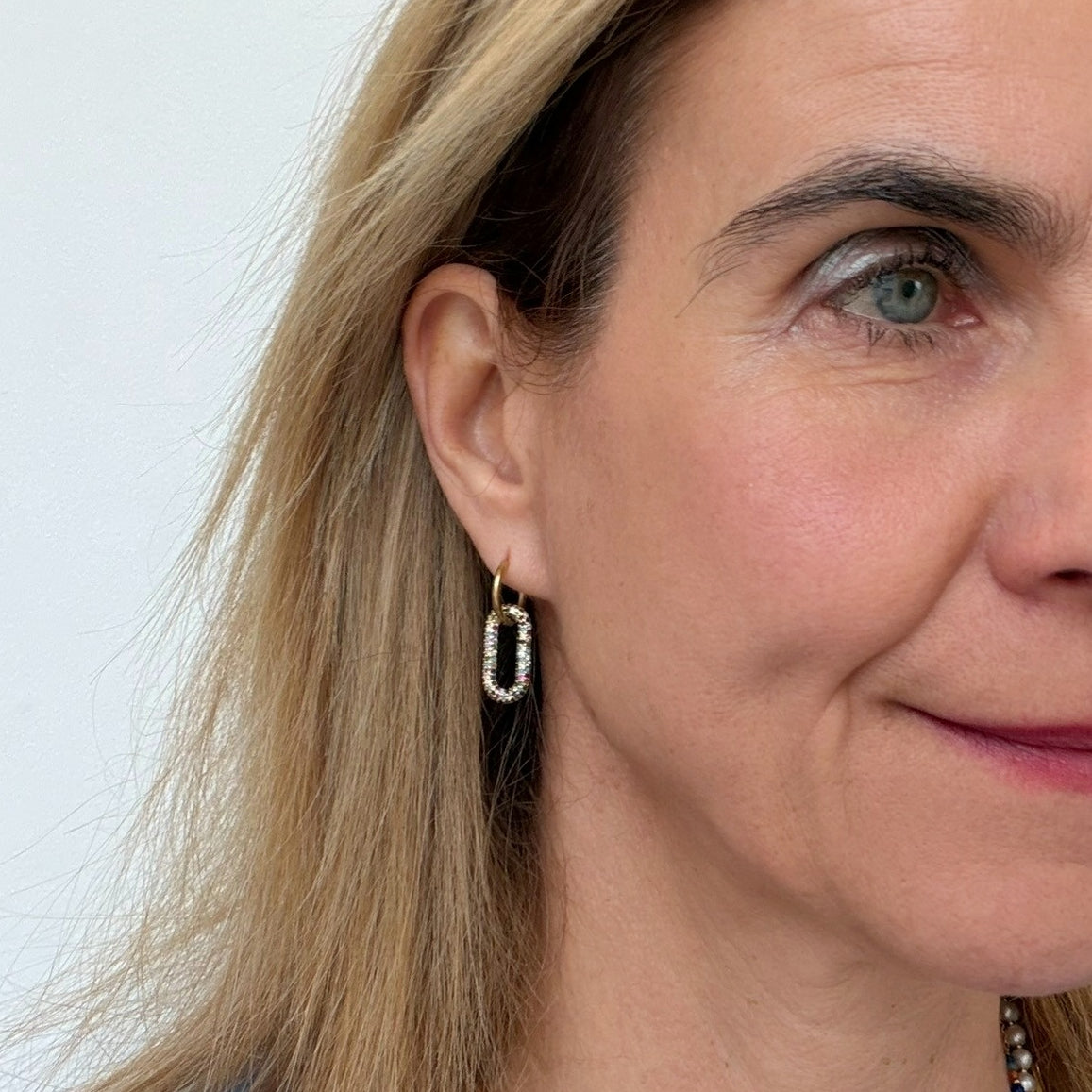 Close-up of a woman wearing a gold hoop earring with a oval shaped charm