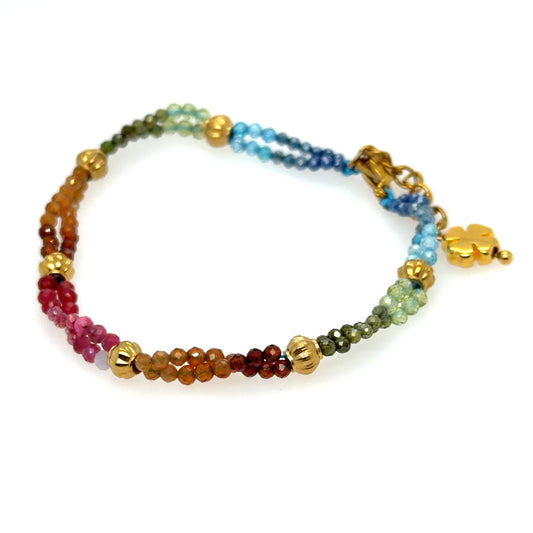 A beaded bracelet featuring a rainbow gradient of faceted gemstone beads separated by gold-toned metallic spacers, with a gold four-leaf clover charm and clasp, shown on a white background.