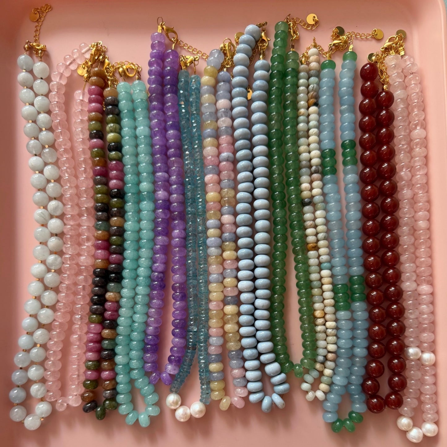 Collection of colourful gemstone rondelle necklaces on a pink background