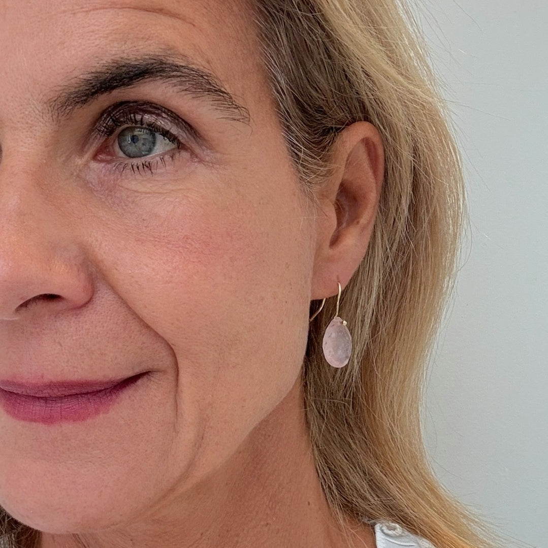 Close-up of a woman wearing a rose quartz teardrop earring against a neutral background