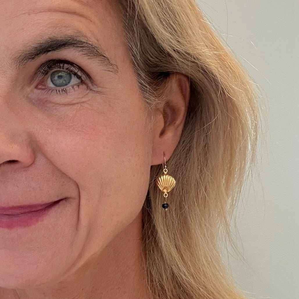 Close-up of a woman wearing gold shell earrings with a dark blue gemstone.