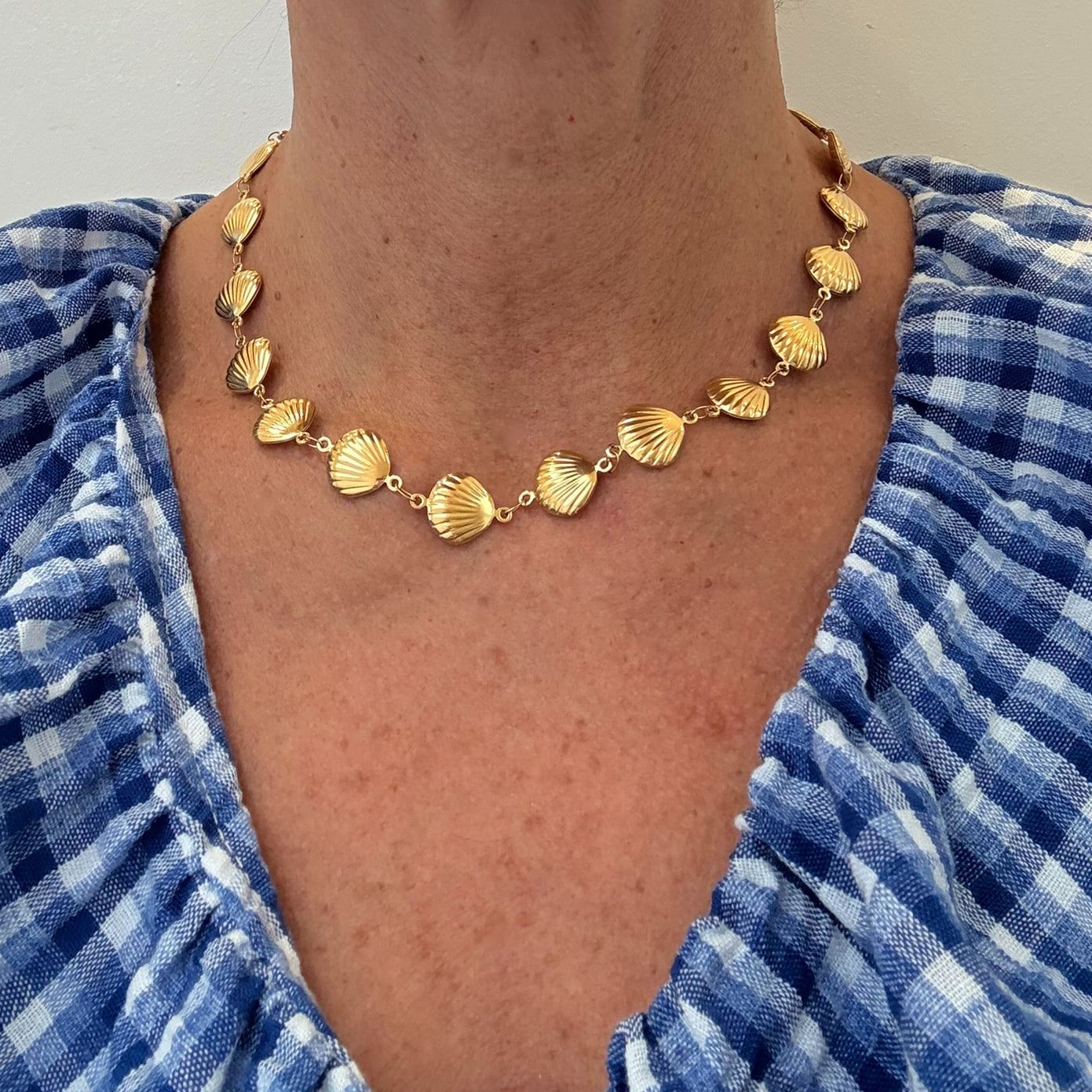 Gold necklace with shell-like pendants on a person wearing a blue and white checkered garment.