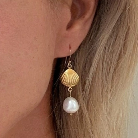 Gold shell and pearl earring worn by a person with blonde hair.