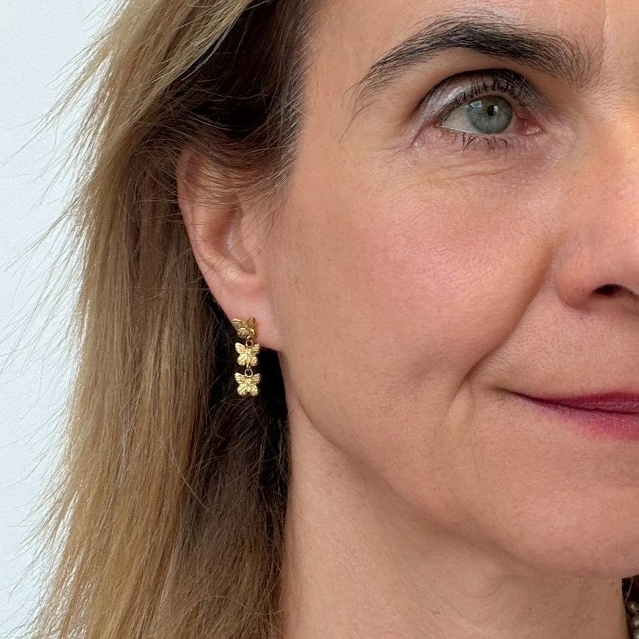 Close-up of a woman wearing gold butterfly earrings with a plain background