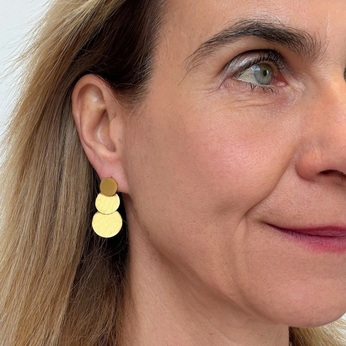 Close-up of a woman wearing gold disc earrings with a neutral background