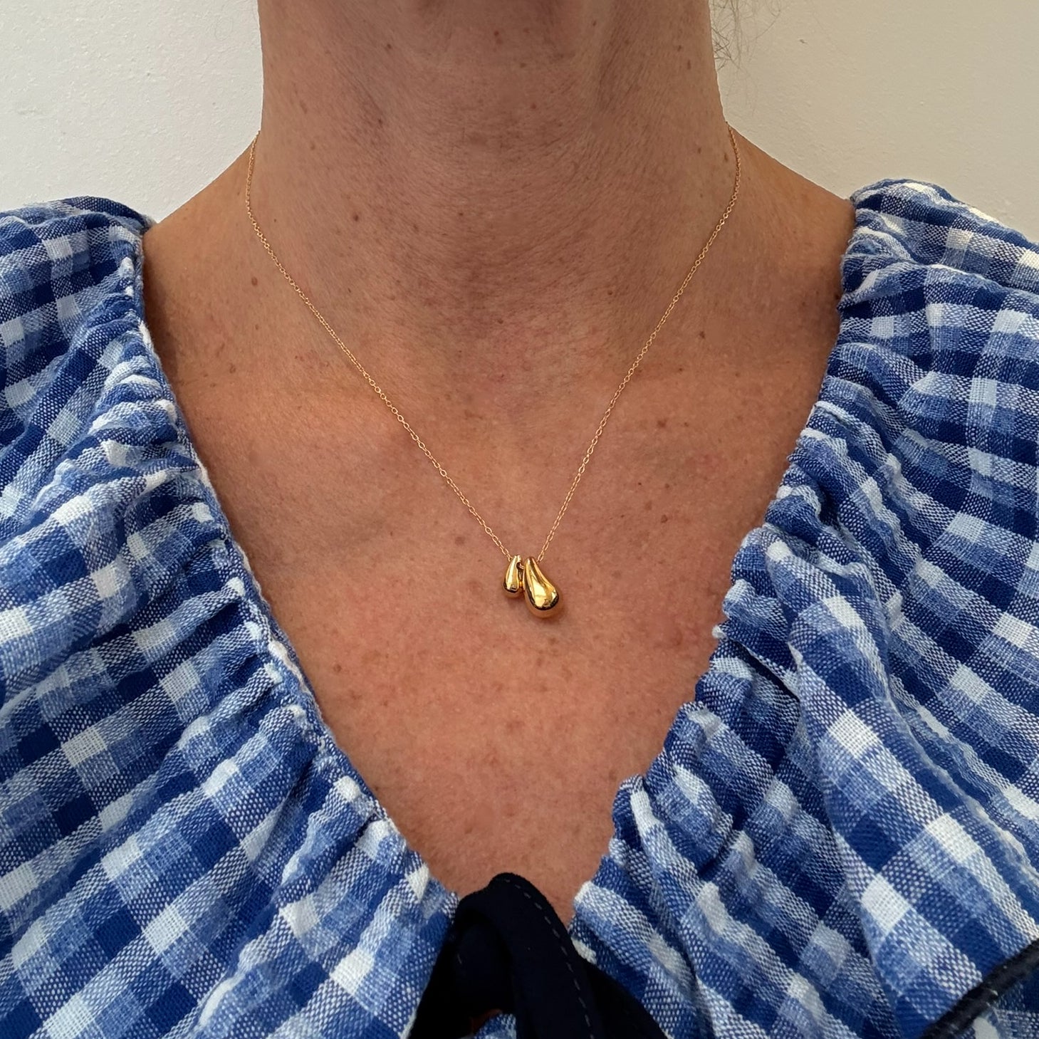 Person wearing a gold necklace with a pendant, dressed in a blue checkered outfit.
