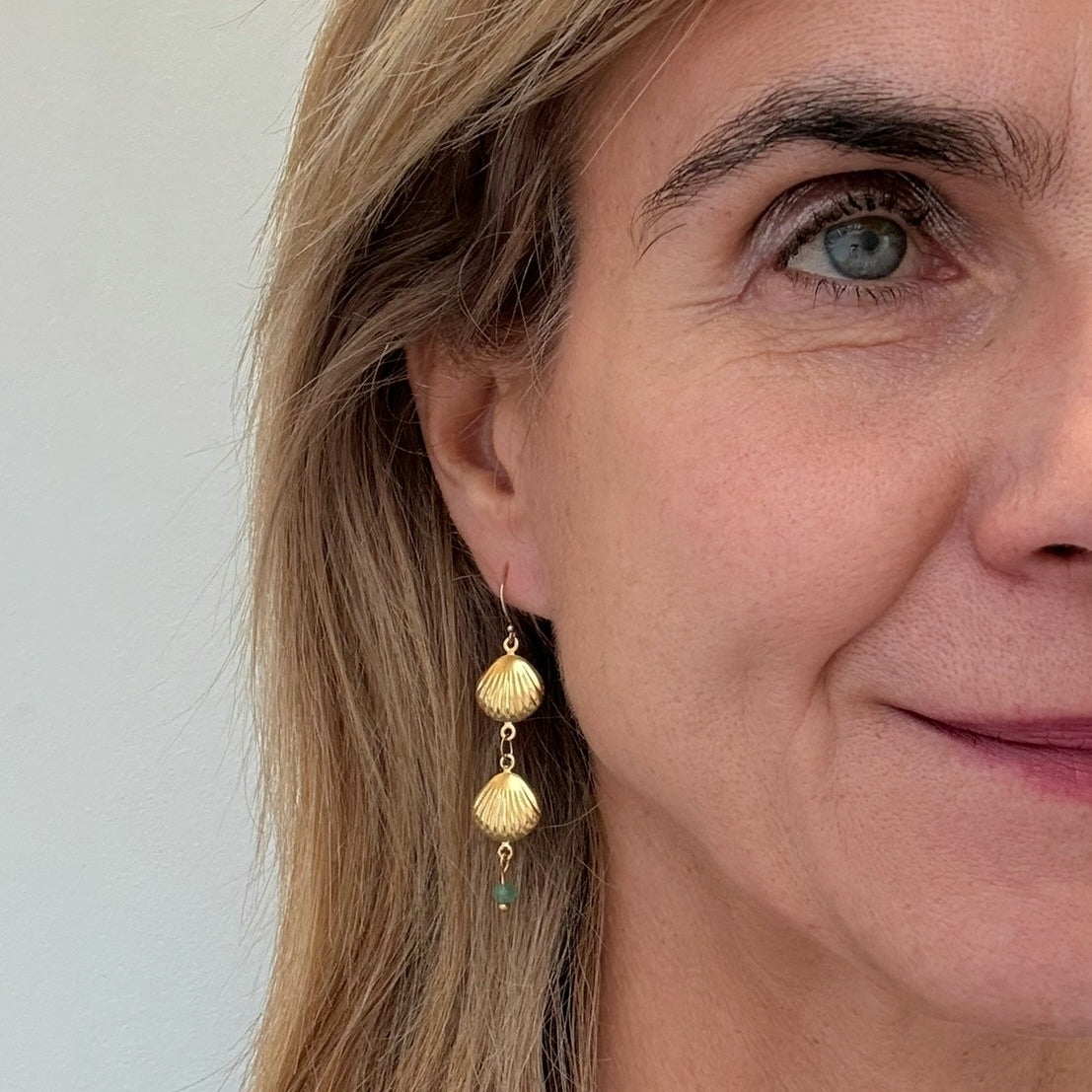 Gold filled ear hooks with two dangling gold shell charms and a tiny green quartz bead worn on  model