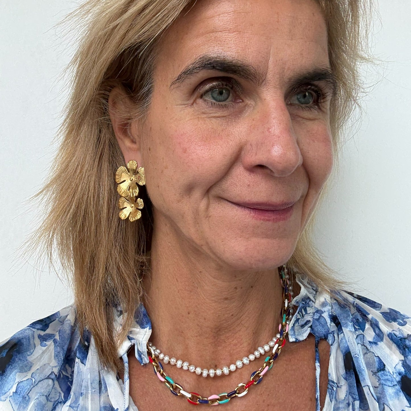 Woman wearing gold flower shaped earrings, pearl necklace and colorful necklace 