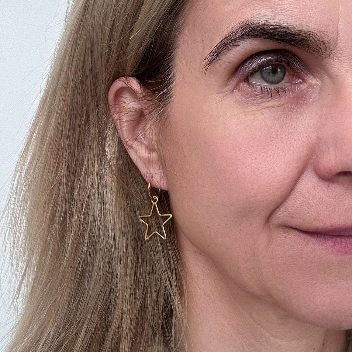 Delicate gold hoop earrings with a large star outline charm worn on woman
