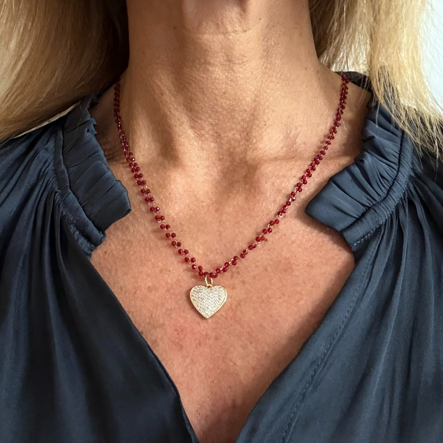 Necklace with two rows of tiny red glass beads and gold sparkly heart charm in the middle worn on model