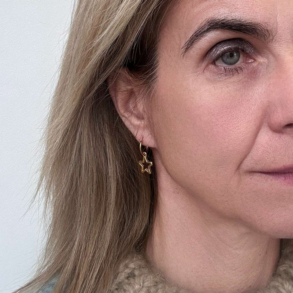 woman wearing gold hoop earrings with small star outline charms