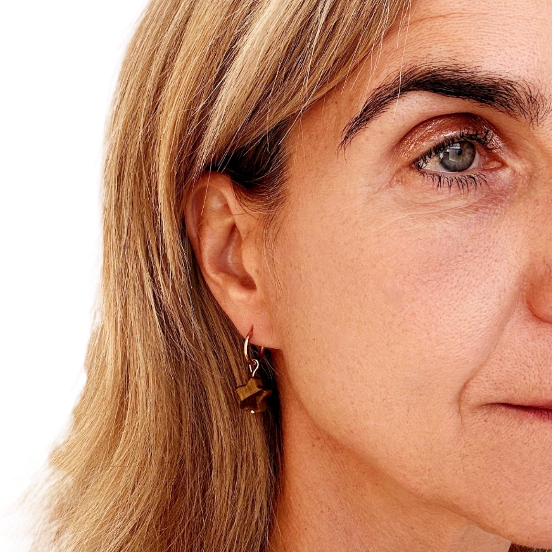 woman wearring gold hoop earrings with star shaped natural Tiger Eye stone charms